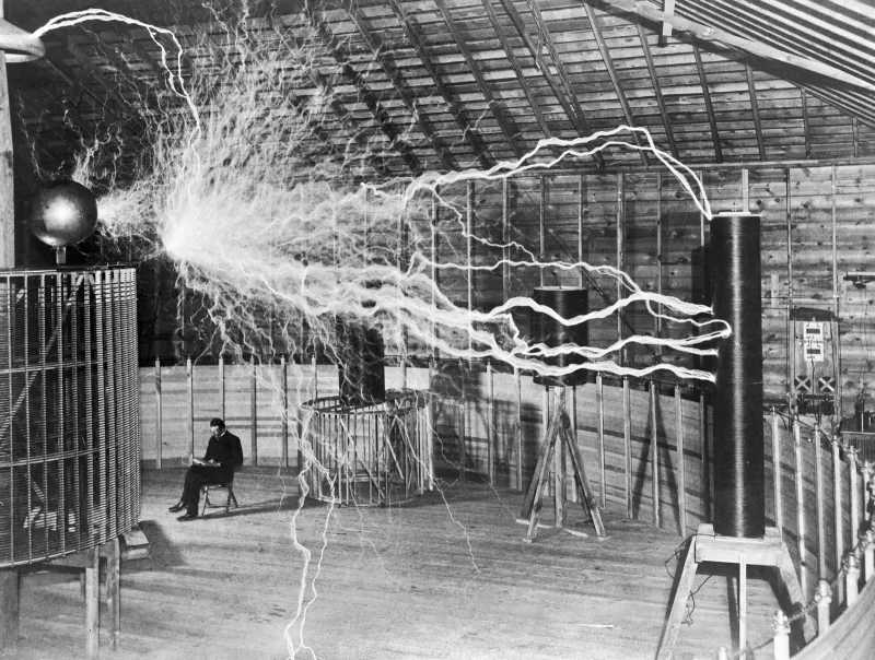 Nikola Tesla seated in his Colorado Springs laboratory beside high-voltage equipment